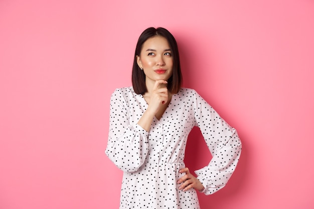 Photo gratuite femme asiatique heureuse réfléchie prenant une décision souriante satisfaite et regardant le logo en haut à gauche pensant...