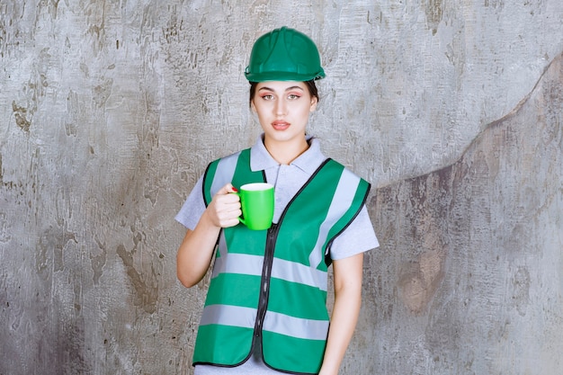 Photo gratuite femme ingénieur en casque vert tenant une tasse de café vert