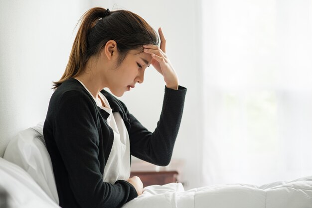 La femme malade avait mal à la tête et les mains touchaient sa tête sur le lit.