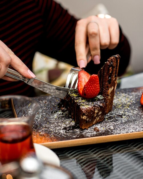 Femme mange un gâteau au chocolat avec des tranches de fraise sur le dessus