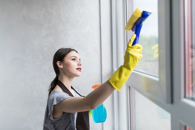 Photo gratuite une femme portant des gants de protection sourit et essuie la poussière à l'aide d'un spray et d'un plumeau tout en nettoyant sa maison, gros plan