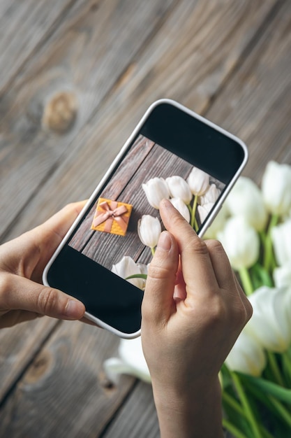 Photo gratuite une femme prend une photo d'un bouquet de tulipes blanches et d'une boîte à cadeaux