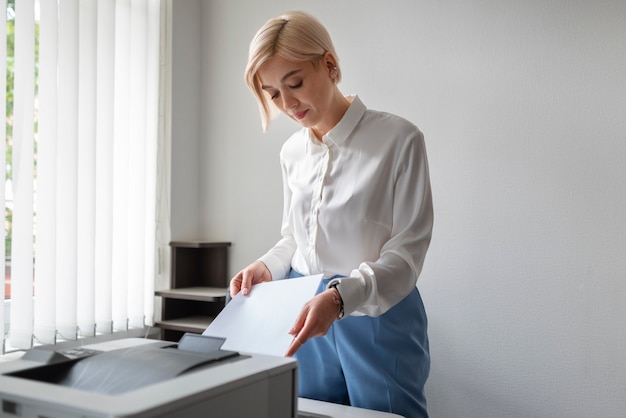 Photo gratuit femme utilisant une imprimante tout en travaillant au bureau