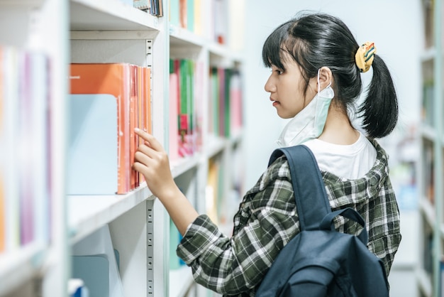 Photo gratuite des femmes portant un sac à dos et recherchant des livres dans la bibliothèque.