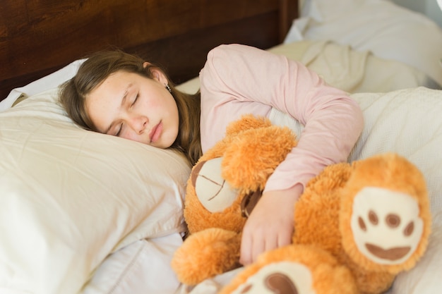 Photo gratuite fille dormant avec un ours en peluche doux sur le lit