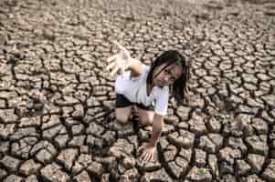 Photo gratuite la fille était assise ailleurs, la main au ciel pour demander la pluie sur le sol sec, le réchauffement climatique