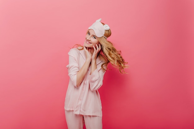 Photo gratuite fille frisée glamour exprimant son énergie le matin. agréable femme caucasienne en pyjama de soie posant sur un mur rose.