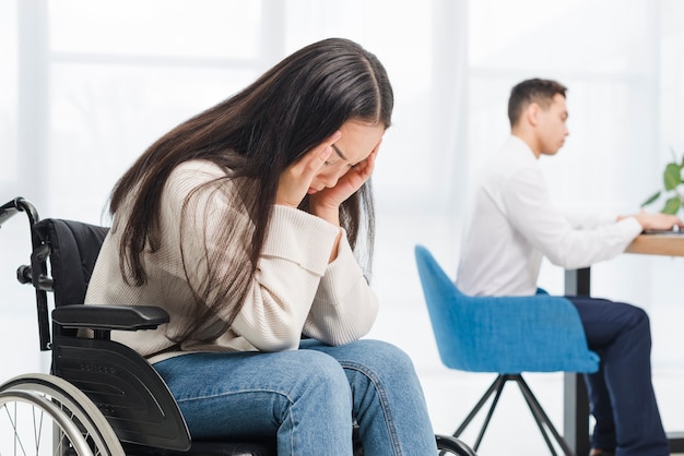 Frustré de jeune femme souffrant de maux de tête assis sur une chaise roulante devant l&#39;homme d&#39;affaires travaillant dans le bureau