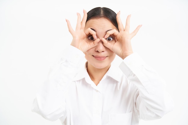 Photo gratuit les gens d'affaires happy asian girl regarde à travers les lunettes de doigt regarde avec visage surpris est isol