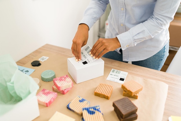 Photo gratuite gros plan sur des mains féminines mettant une étiquette d'expédition sur un colis contenant des produits naturels de beauté et organisant les commandes des clients en ligne