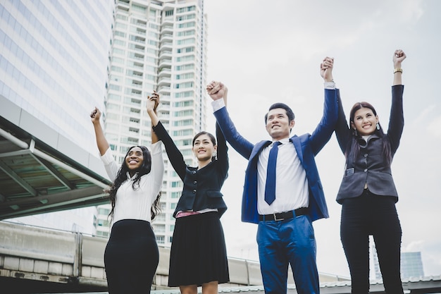 Photo gratuite groupe de jeunes entrepreneurs heureux avec les mains dans les airs succès sur leurs plans.