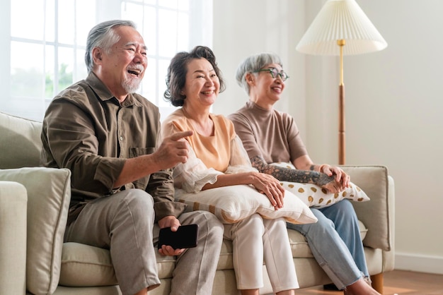 Photo gratuite groupe de vieux hommes et femmes seniors asiatiques passant le week-end ensemble s'asseoir sur un canapé-lit en regardant une émission de comédie télévisée avec un rire joyeux souriant des expressions de bonheur des personnes âgées dans une maison de retraite