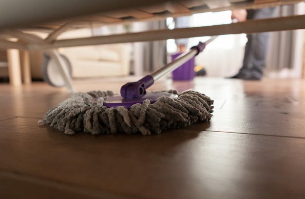 Photo gratuite guy épongeant la poussière sous le canapé dans l'appartement