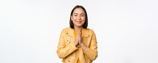 Photo gratuite heureuse femme coréenne à la recherche d'espoir demandant de l'aide en faveur de la mendicité debout avec un geste de namaste et souriant debout sur fond blanc