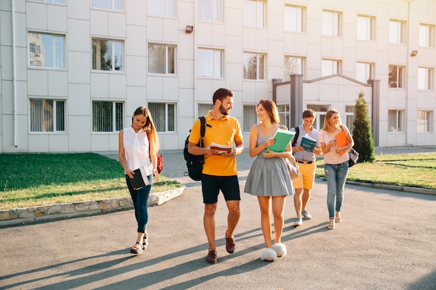 Photo gratuite heureux étudiants avec des livres en mains marchant ensemble sur le campus