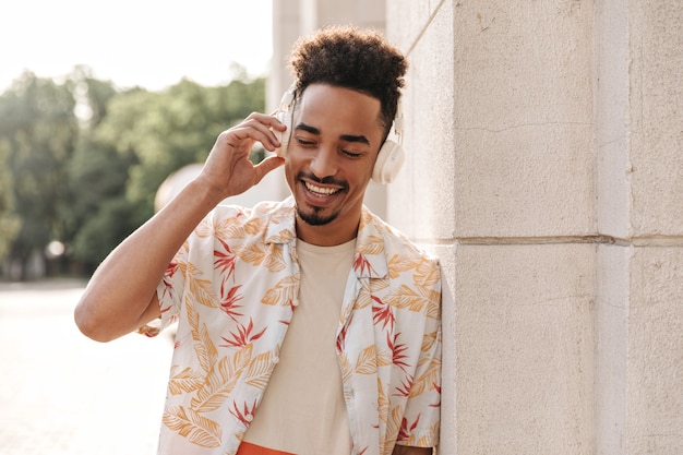 Photo gratuite heureux homme brunet à la peau foncée en chemise à fleurs sourit avec les yeux fermés