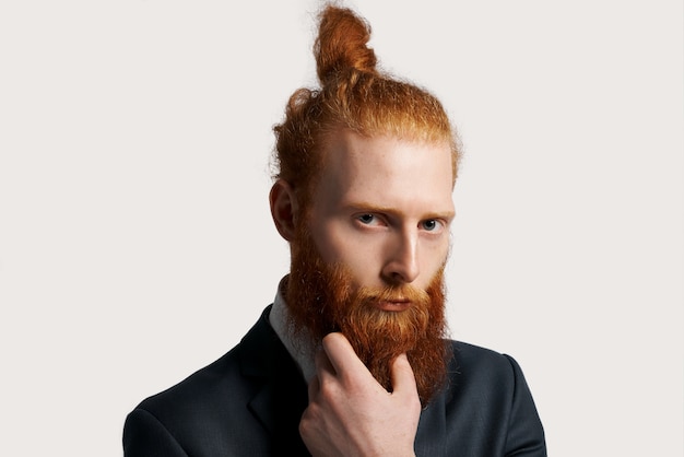 Photo gratuite homme d'affaires efficace et talentueux aux cheveux roux avec une forte vue et tenir sa barbe à la main