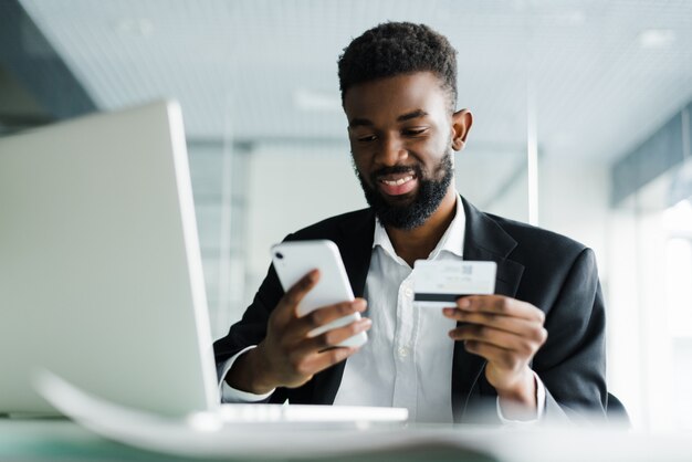 Homme afro-américain payer avec une carte de crédit en ligne tout en passant des commandes via Internet mobile faisant une transaction à l'aide d'une application bancaire mobile.