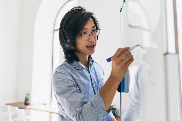 Photo gratuit homme asiatique concentré en chemise bleue à l'aide de flipchart et marqueur pour le travail