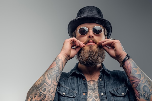 Photo gratuite homme barbu sérieux en chapeau et lunettes de soleil pose au studio photo.