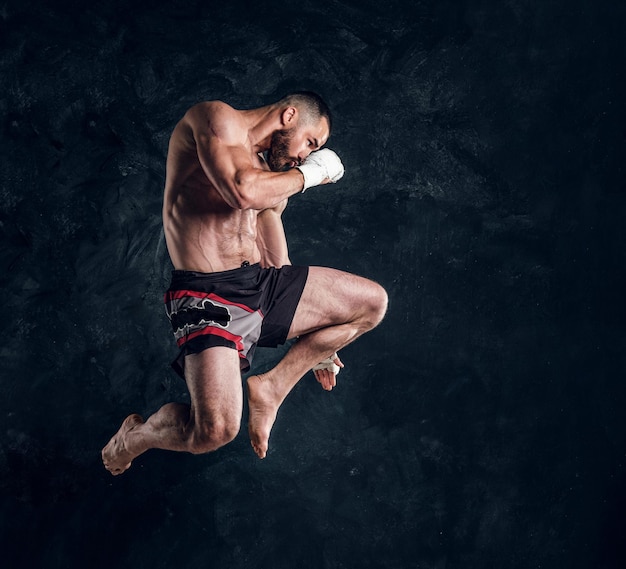 Photo gratuite un homme en bonne forme physique concentré saute, faisant illusion de vol avant de frapper un studio sombre.