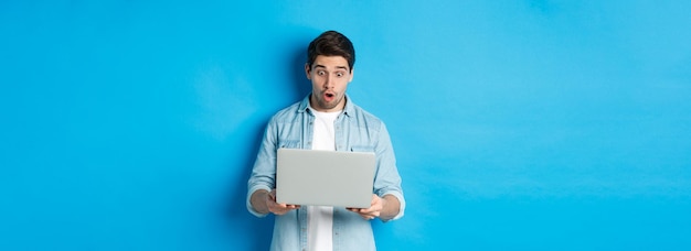 Photo gratuite un homme caucasien impressionné regardant un écran d'ordinateur portable avec étonnement en vérifiant la promotion sur le stand internet