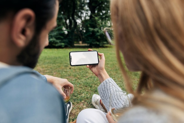 Homme et femme regardant un téléphone tout en ayant un pique-nique en plein air