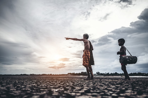 Un homme et un garçon âgés découvrent du poisson sur un sol sec et le réchauffement climatique