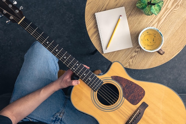 Photo gratuite un homme avec une guitare acoustique et un bloc-notes avec une tasse sur la table