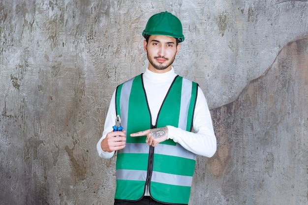 Photo gratuite homme ingénieur en uniforme jaune et casque tenant une pince bleue pour réparation.