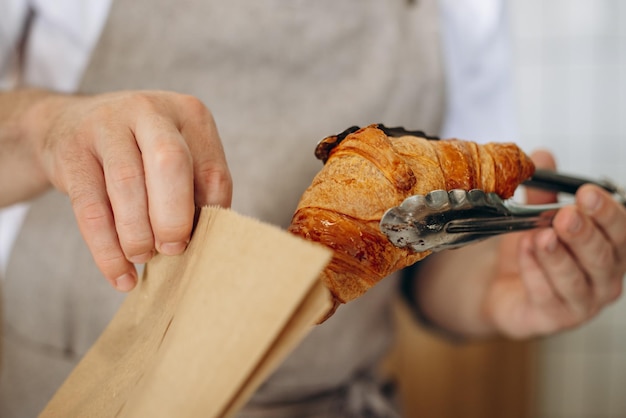 L'homme met un croissant dans un sac en papier à l'aide de pinces