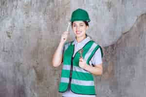 Photo gratuite ingénieur en casque vert tenant une clé métallique pour un travail de réparation et a l'air confus et réfléchi.