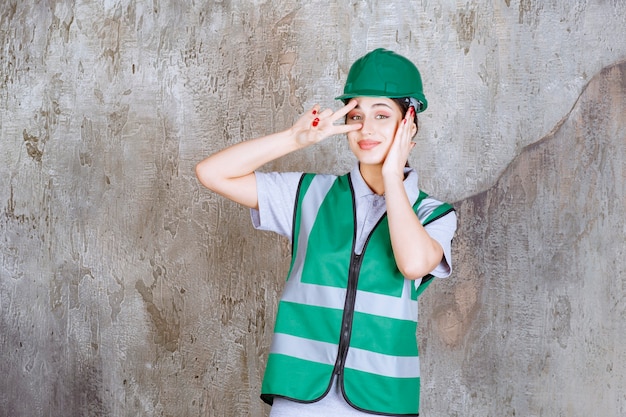 Photo gratuite ingénieur féminin en uniforme vert et casque envoyant la paix et l'amitié