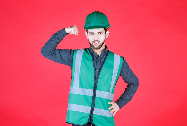 Photo gratuite ingénieur en uniforme vert et casque démontrant son poing.