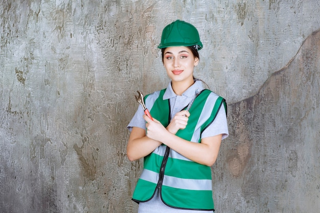 Photo gratuite ingénieure en casque vert tenant une clé métallique pour un travail de réparation.