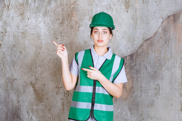 Photo gratuite ingénieure en uniforme vert et casque montrant le côté gauche avec émotions.