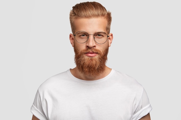 Photo gratuite jeune bel homme hipster a une barbe et une moustache épaisses au gingembre, une coupe de cheveux à la mode, vous regarde sérieusement