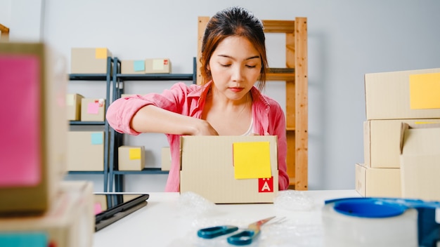 Photo gratuite jeune femme d'affaires entrepreneur asie produit d'emballage dans une boîte en carton livrer au client, travaillant au bureau à domicile. propriétaire de petite entreprise, démarrez la livraison du marché en ligne, concept indépendant de style de vie.