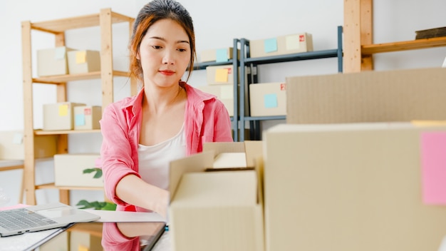 Photo gratuite jeune femme d'affaires entrepreneur en asie vérifier le bon de commande du produit en stock et enregistrer sur ordinateur portable au bureau à domicile propriétaire de petite entreprise, livraison de marché en ligne, concept indépendant de style de vie.