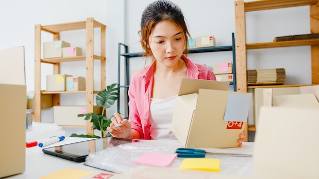 Photo gratuite jeune femme d'affaires entrepreneur en asie vérifier le bon de commande du produit en stock et enregistrer sur le travail de l'ordinateur tablette au bureau à domicile. propriétaire de petite entreprise, livraison de marché en ligne, concept indépendant de style de vie.