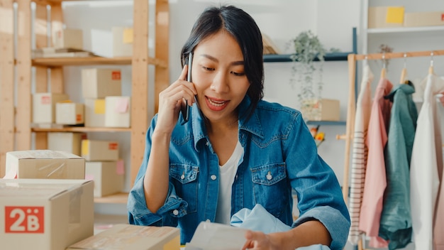 Photo gratuite jeune femme asiatique à l'aide de smartphone recevant un bon de commande et vérifiant le produit sur le travail en stock au bureau à domicile