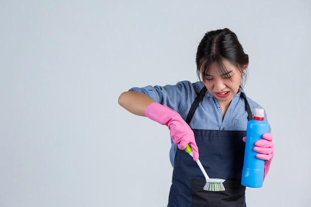 Photo gratuite jeune femme au foyer porte des gants jaunes lors du nettoyage avec le produit de nettoyage sur mur blanc.