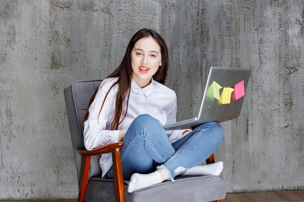 Photo gratuit jeune femme concentrée assise sur un fauteuil travaillant sur un ordinateur portable. photo de haute qualité