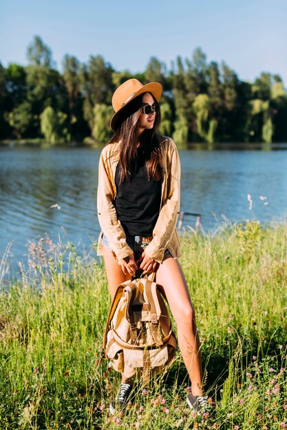 Jeune femme élégante, debout près de la rivière avec le sac à dos