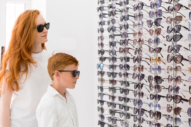 Photo gratuite jeune femme et garçon debout ensemble dans la salle d'exposition d'optique