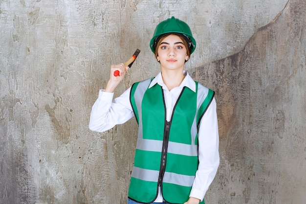 Photo gratuite jeune femme ouvrier du bâtiment en casque vert posant avec un marteau