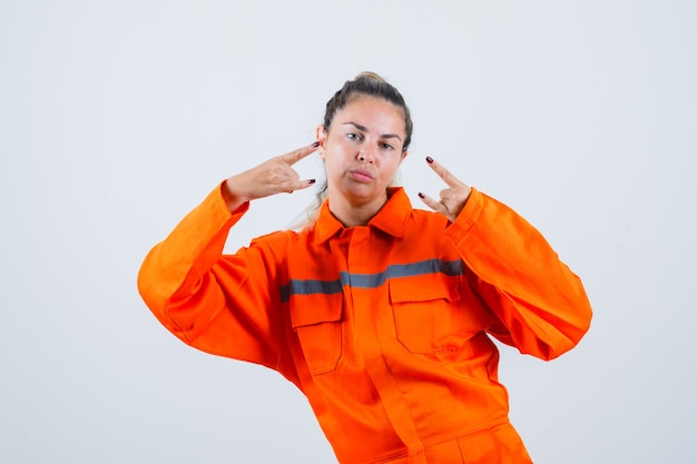 Photo gratuite jeune femme en uniforme de travailleur faisant du rock en symbole de rouleau avec les mains et à la vue de face, assuré.