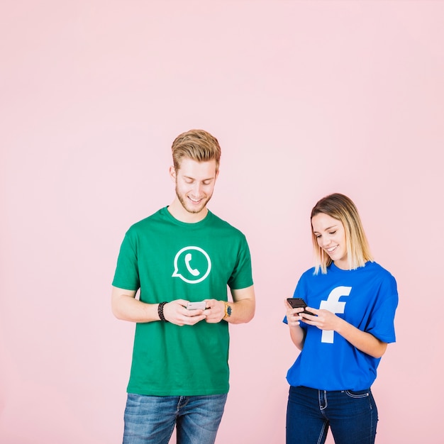 Photo gratuite jeune homme et femme à l'aide de téléphone portable sur fond rose