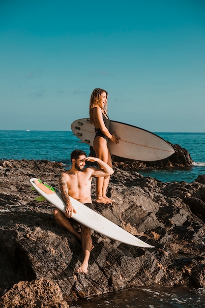 Photo gratuite jeune homme et une femme surprise avec des planches de surf sur le rocher près de la mer