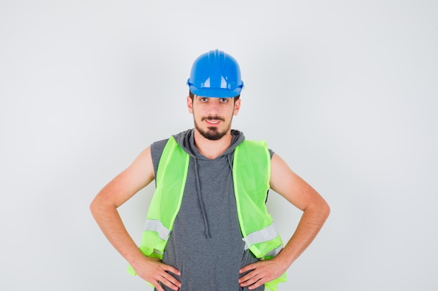 Photo gratuite jeune homme tenant les mains sur la taille en uniforme de construction et l'air heureux